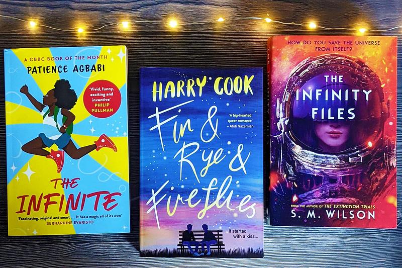 The Infinite by Patience Agbabi, Fin & Rye & Fireflies by Harry Cook and The Infinity Files by S.M Wilson lined up beside fairy lights